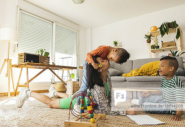 Playful son kissing mother lying on carpet at home