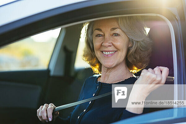Happy mature woman fastening seat belt in car