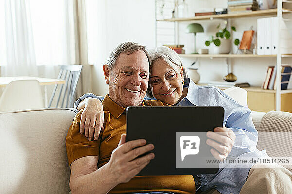 Glückliches älteres Paar  das zu Hause auf dem Sofa sitzt und auf einen Tablet-PC blickt
