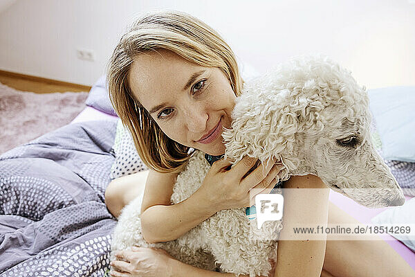 Smiling naked woman hugging Poodle dog at home