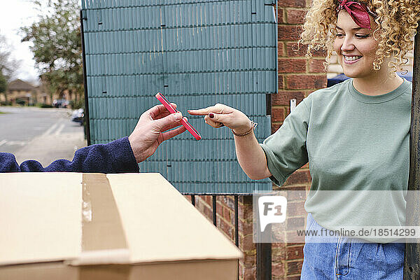 Happy woman touching smart phone held by delivery person