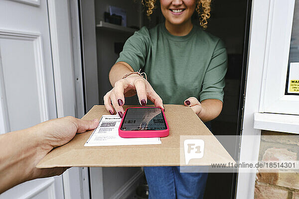 Happy woman using smart phone and taking delivery of package