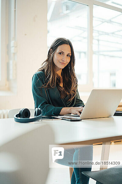 Smiling businesswoman sitting with laptop at home office