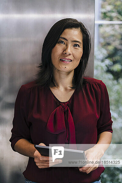 Smiling businesswoman standing with tablet PC in office