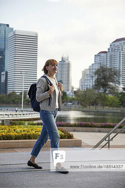 Mature businesswoman wearing backpack walking on footpath