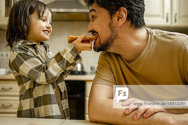Happy boy feeding pizza to father at home