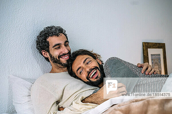 Happy gay couple relaxing together on bed at home