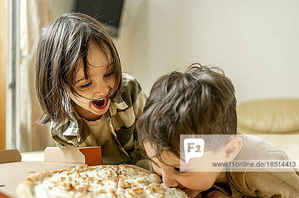 Cheerful siblings having pizza at home