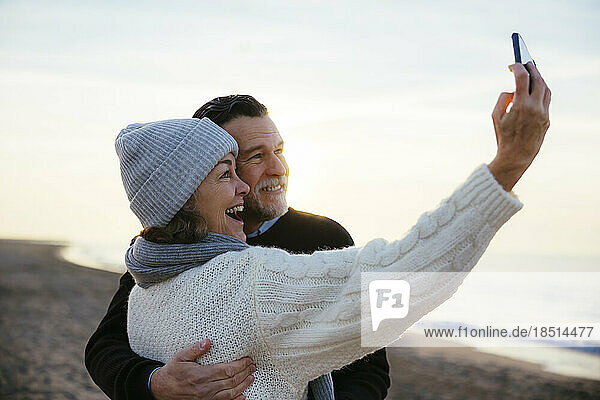 Happy mature woman taking selfie with man at beach