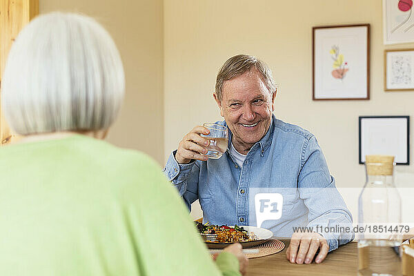 Smiling senior man with glass of water enjoying lunch at home