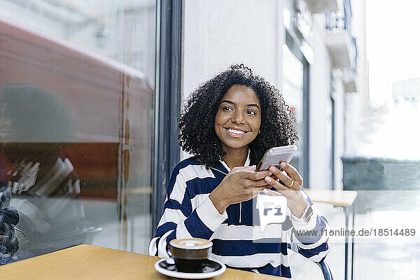 Happy woman with smart phone sitting at table of sidewalk cafe