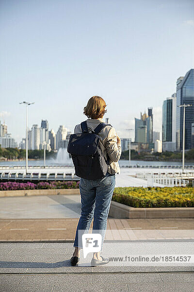 Businesswoman wearing backpack looking at buildings standing on footpath