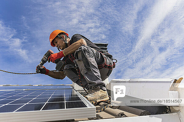 Technician using drill machine and installing solar panels on roof