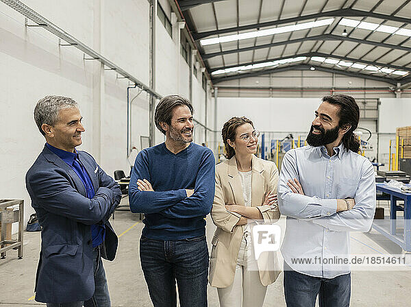 Happy business colleagues standing with arms crossed in factory