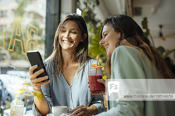 Happy woman sharing smart phone with friend in cafe