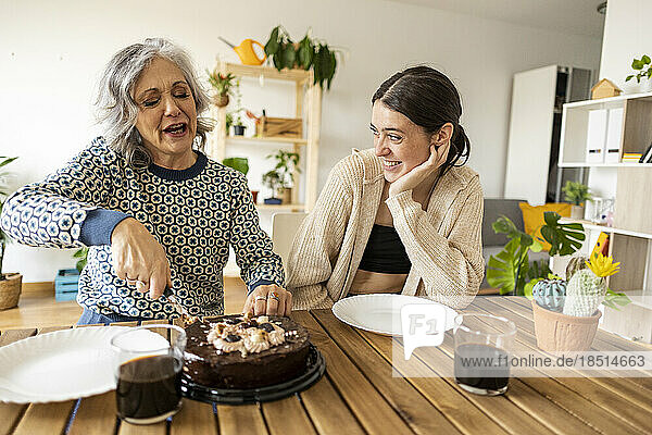 Mother cutting cake with daughter sitting at table