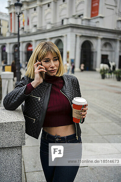 Frau spricht am Smartphone und hält eine Einweg-Kaffeetasse in der Hand