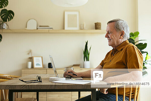 Lächelnder älterer Mann sitzt mit Laptop am Tisch im Büro