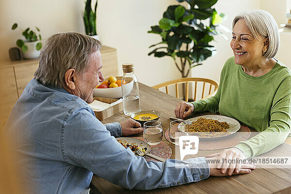 Happy senior couple with stacked hands having lunch at home