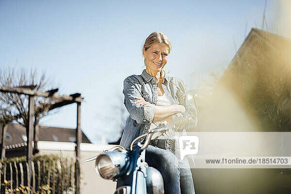 Smiling mature woman sitting with arms crossed on motor cycle