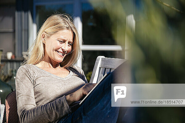 Lächelnder Freiberufler mit Tablet-PC  der an einem sonnigen Tag im Vorgarten sitzt