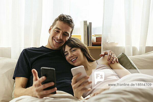 Glückliches Paar mit Smartphones entspannt sich zu Hause im Bett