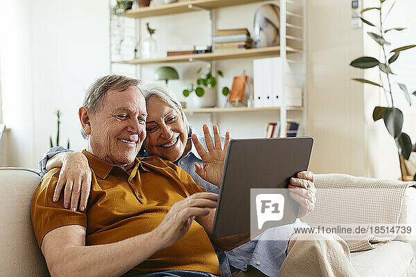 Glückliches älteres Paar gestikuliert bei einem Videoanruf über einen Tablet-PC zu Hause