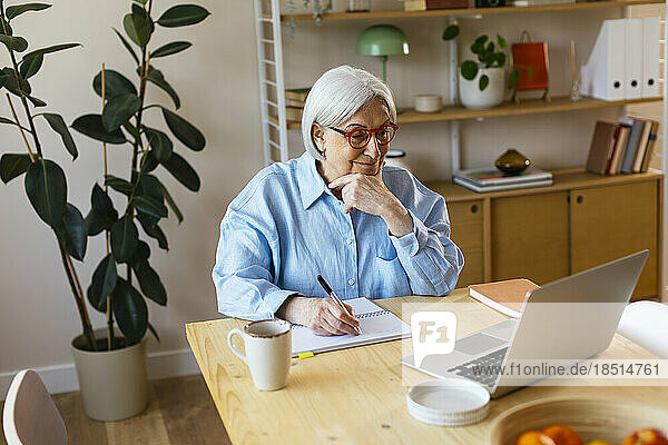 Lächelnde Frau schreibt zu Hause Notizen vom Laptop aus