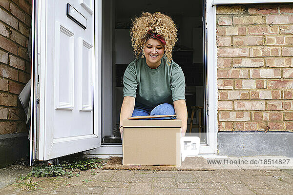 Happy young woman picking up packages from doorway