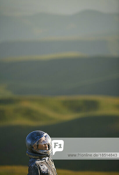 Contemplative woman wearing space helmet in front of landscape