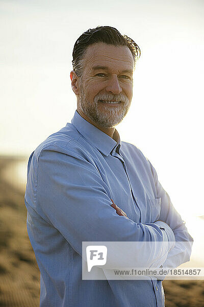 Smiling mature man standing with arms crossed at beach
