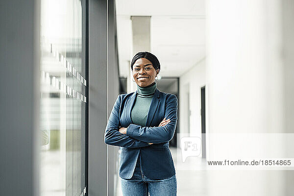 Smiling businesswoman with arms crossed standing near window at office
