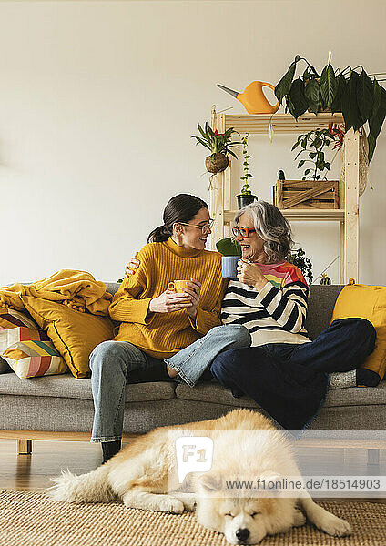 Smiling mother and daughter with coffee cup spending leisure time together at home