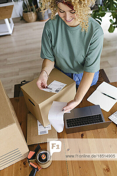 Smiling young woman with shipping label at desk