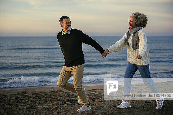 Happy mature couple holding hands and running at beach