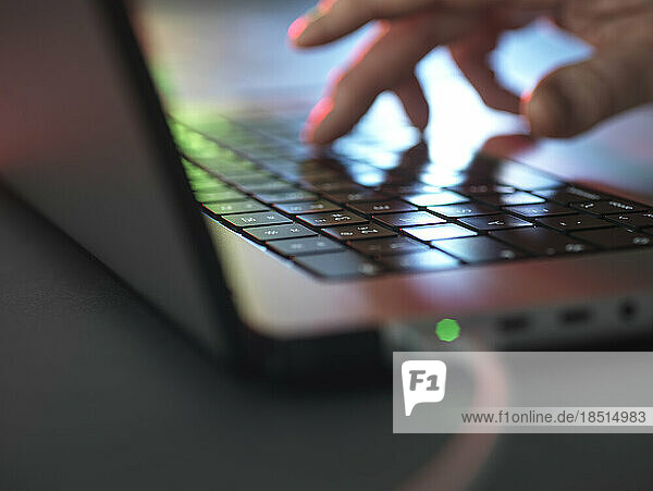 Hands typing on illuminated laptop keyboard in dark at home office