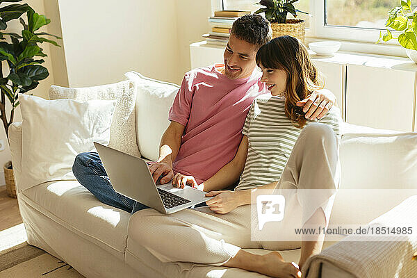 Smiling couple using laptop sitting on sofa at home