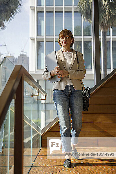Businesswoman with laptop walking on footbridge