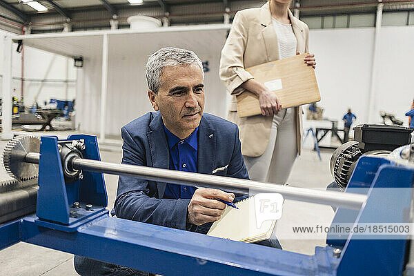 Businessman with note pad examining machine in industry