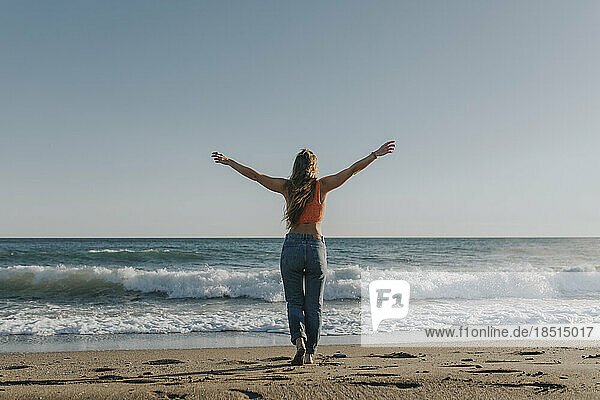 Carefree woman standing with arms outstretched in front of sea