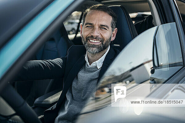 Happy businessman sitting in electric car