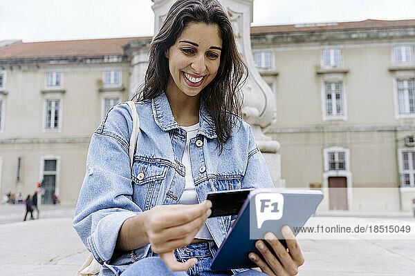 Happy young woman paying through credit card on tablet PC