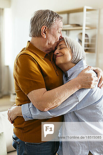 Älterer Mann küsst Frau zu Hause auf die Stirn