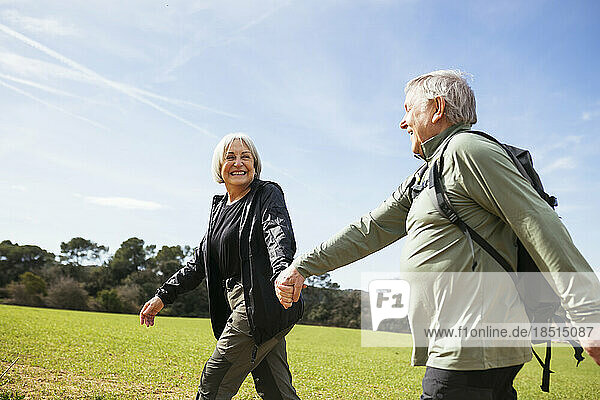 Glückliches älteres Paar  das an einem sonnigen Tag Händchen haltend gemeinsam wandert