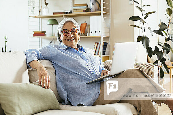 Happy woman sitting with laptop on sofa at home