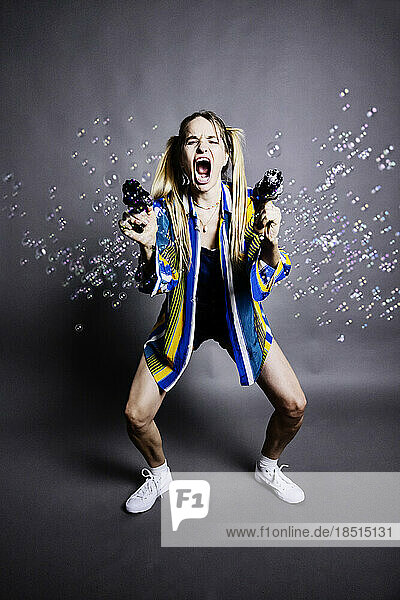 Woman shooting bubbles with guns against gray background
