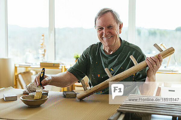 Smiling senior man paining wood in workshop