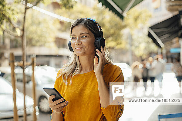 Smiling woman wearing headphones listening to music on footpath