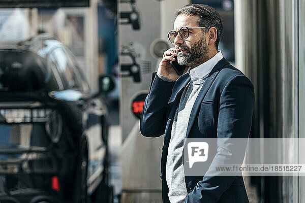 Businessman talking on smart phone standing at car wash