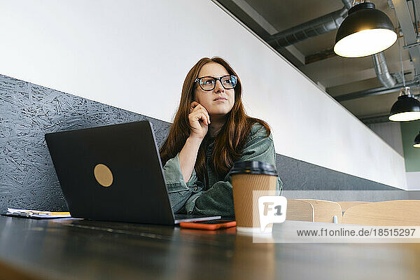 Thoughtful freelancer sitting with laptop at table